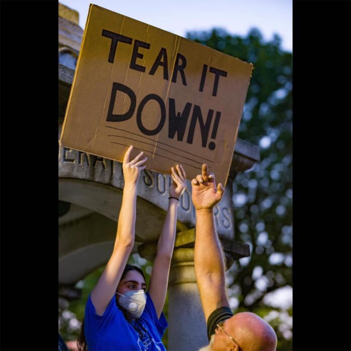 A young woman stands in front of the Murray's Confederate monument as a man makes a lewd gesture at her sign. (Photo by Dave Thompson/Paducah Sun)